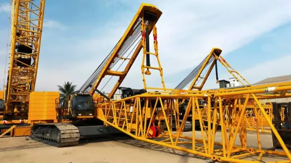 Mobile Crane vs Crawler Crane: How to Choose the Right One for Your Lift 2 Large yellow crawler crane lattice boom and counterweights being assembled by a service crew on a construction site.