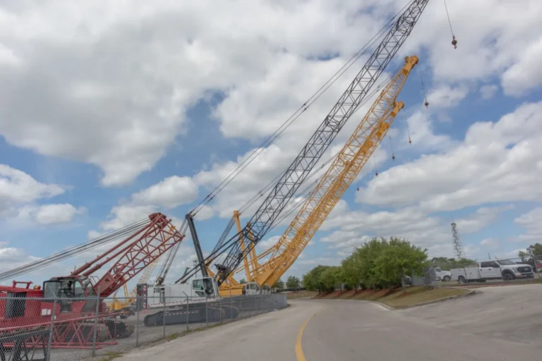 Blog 1 Several large crawler crane lattice booms lined up on a gravel construction site under a cloudy sky.